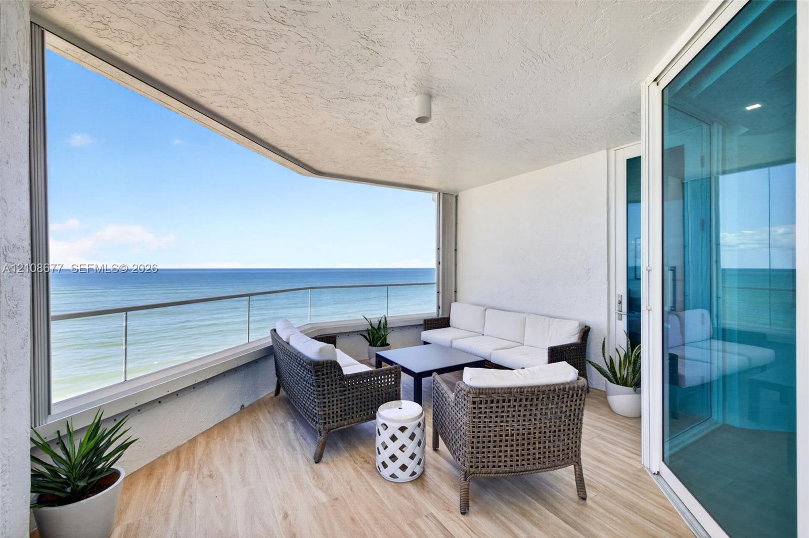 Covered balcony featuring the same wood look plank porcelain flooring as interior, a frameless glass railing, and expansive ocean scenery. Additional protection for your furniture with upgraded accordion shutters.