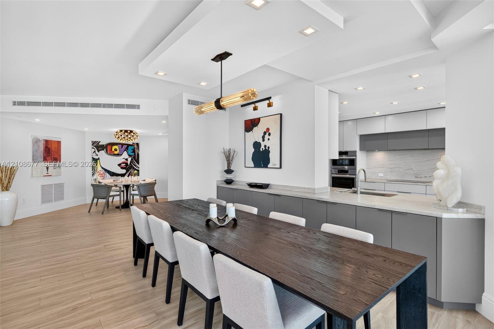 Open-concept dining space space featuring wood look plank porcelain flooring, a coffered ceiling with recessed lighting, minimalist flat-panel cabinets, stone counters, and a beautiful modern pendant fixture. Great open pass through to the kitchen and sink, amazing buffet / storage space Open-concept dining space space featuring wood look plank porcelain flooring, a coffered ceiling with recessed lighting, minimalist flat-panel cabinets, stone counters, and a beautiful modern pendant fixture. Great open pass through to the kitchen and sink, amazing buffet / storage space