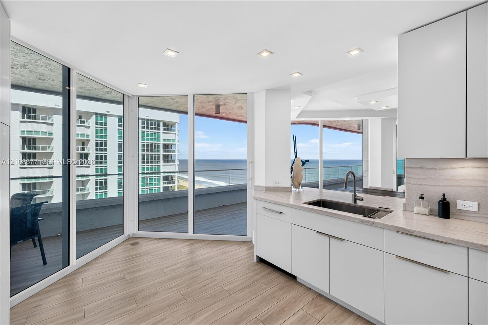Kitchen featuring flat-panel white cabinets, stone counters, undermount sink with a beautiful gooseneck faucet, wood look plank porcelain flooring, and floor-to-ceiling windows with balcony access for morning sunrise breakfast.