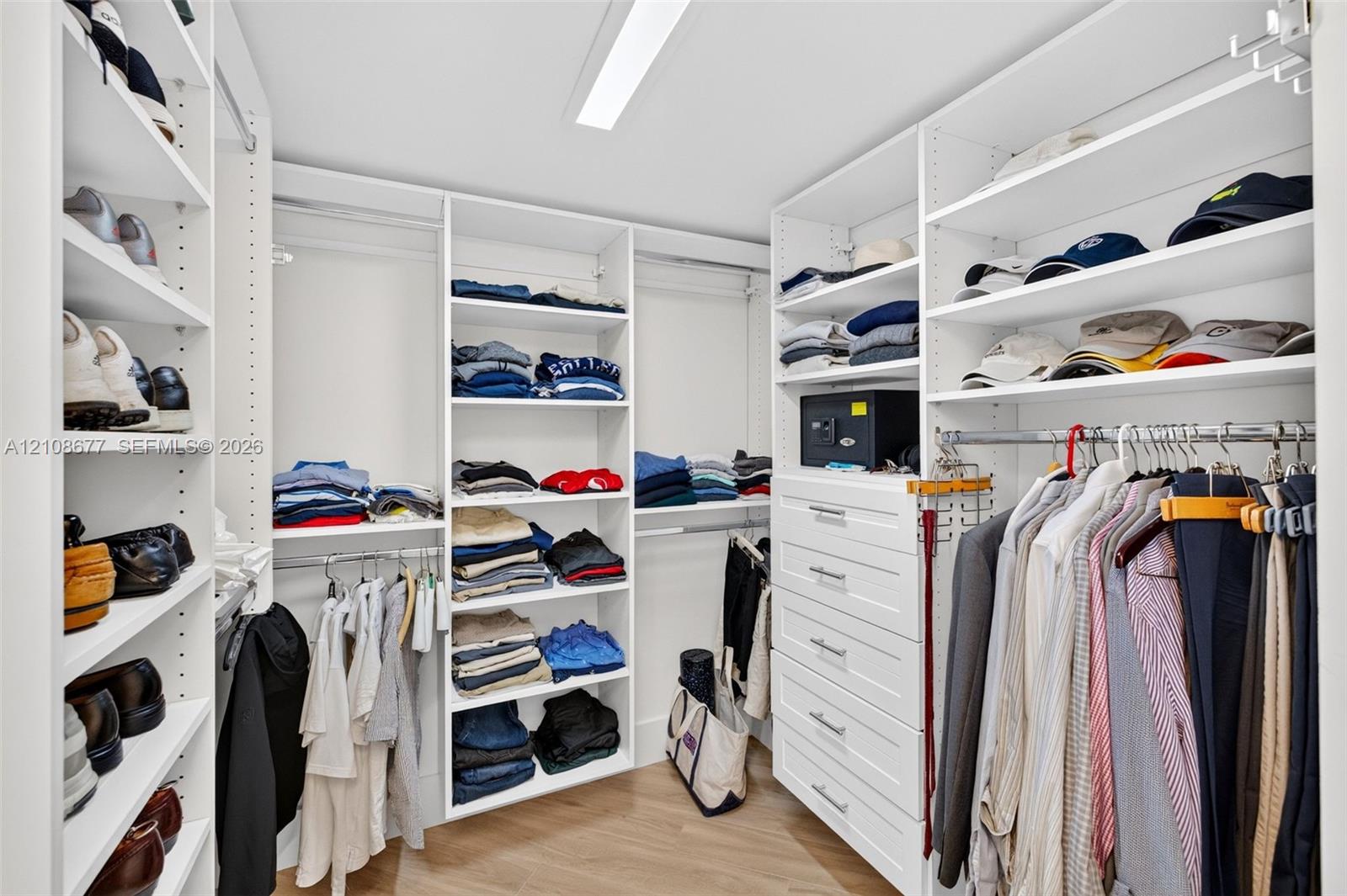 View toward shorter side of the custom walk-in closet featuring floor-to-ceiling white shelving, integrated clothing rods, stacked drawer storage, and wood look plank porcelain flooring
