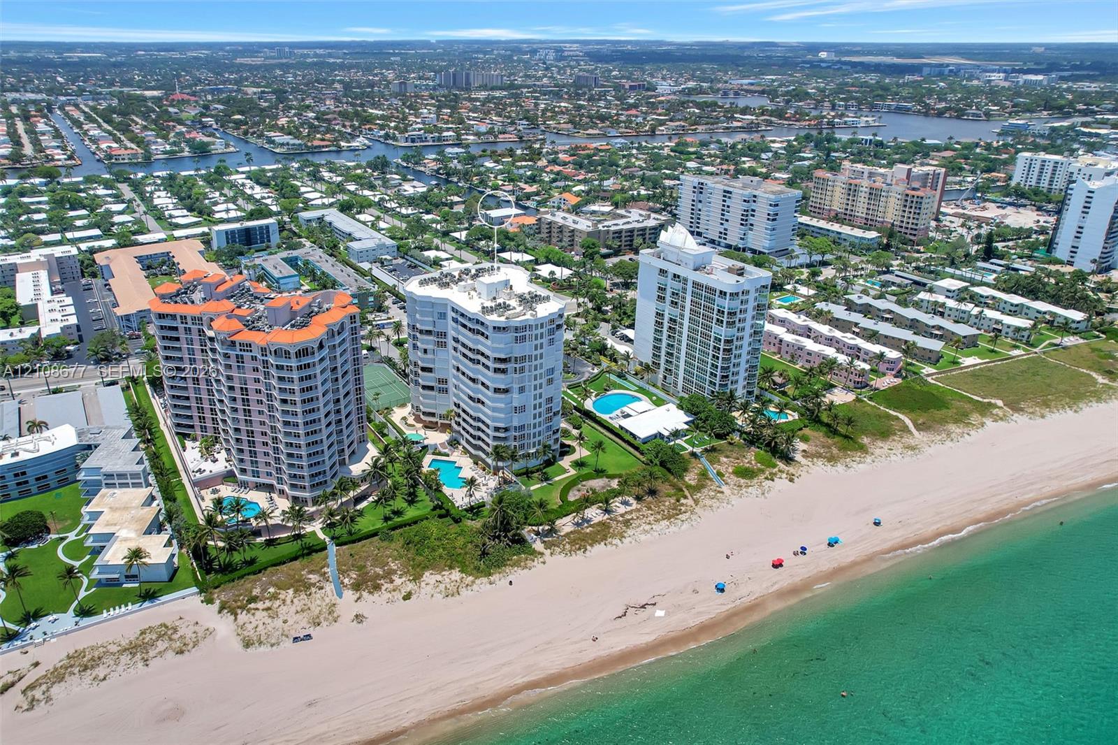 Aerial perspective of coastal high-rise condominiums featuring direct beachfront access, expansive sandy shoreline, outdoor swimming pools, and manicured landscaped grounds