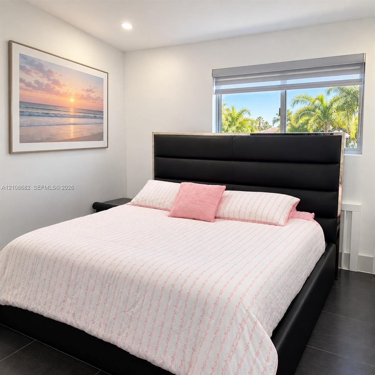 Neutral-toned walls, dark tiled flooring, and a window with roller-style shade featuring palm tree exterior scenery