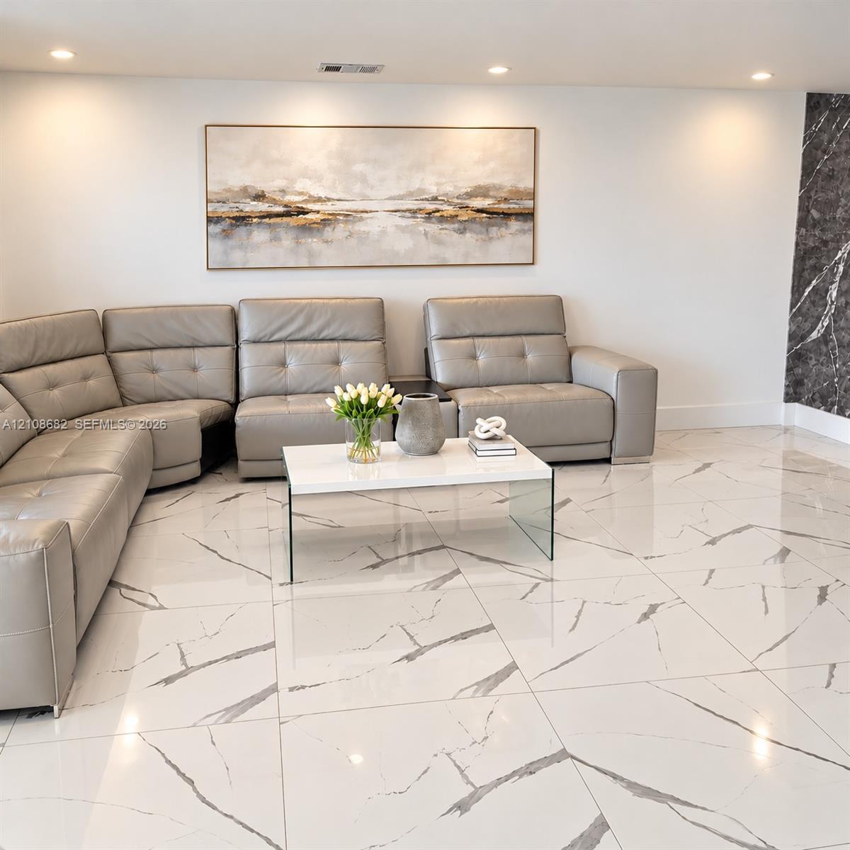Polished large-format floor tiles featuring a white base with dark veining, recessed ceiling lighting, and a dark stone-finish accent wall