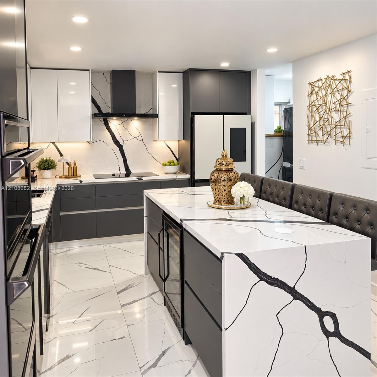 Contemporary kitchen featuring a waterfall-edge island with stone-finish surfaces, dual-tone cabinetry, a matching stone-finish full-height backsplash, recessed lighting, and an integrated wine refrigerator