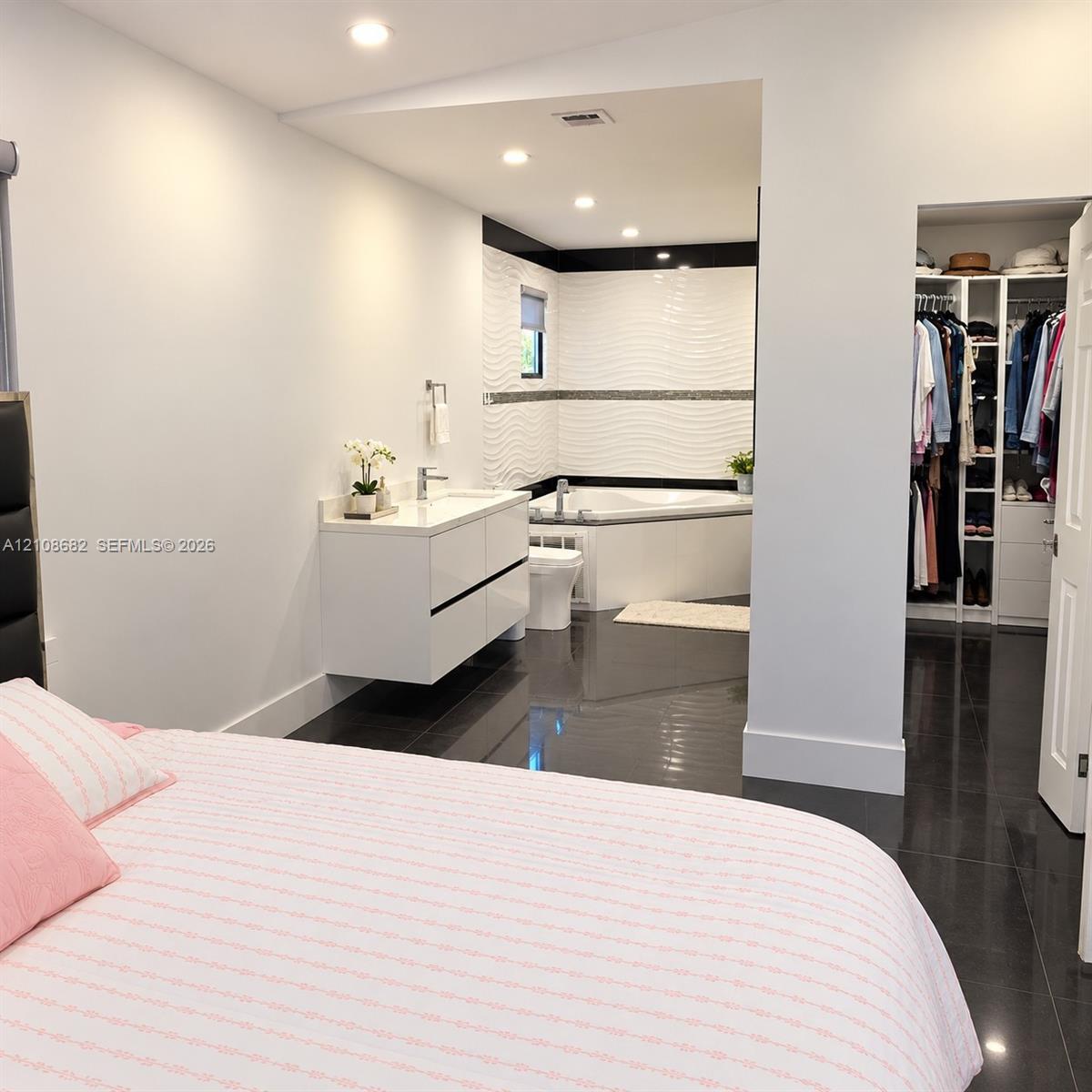 Glossy tile flooring, wall-mounted double-drawer vanity with white countertop, soaking tub with textured tile surround, and walk-in closet featuring custom built-in shelving and organizers