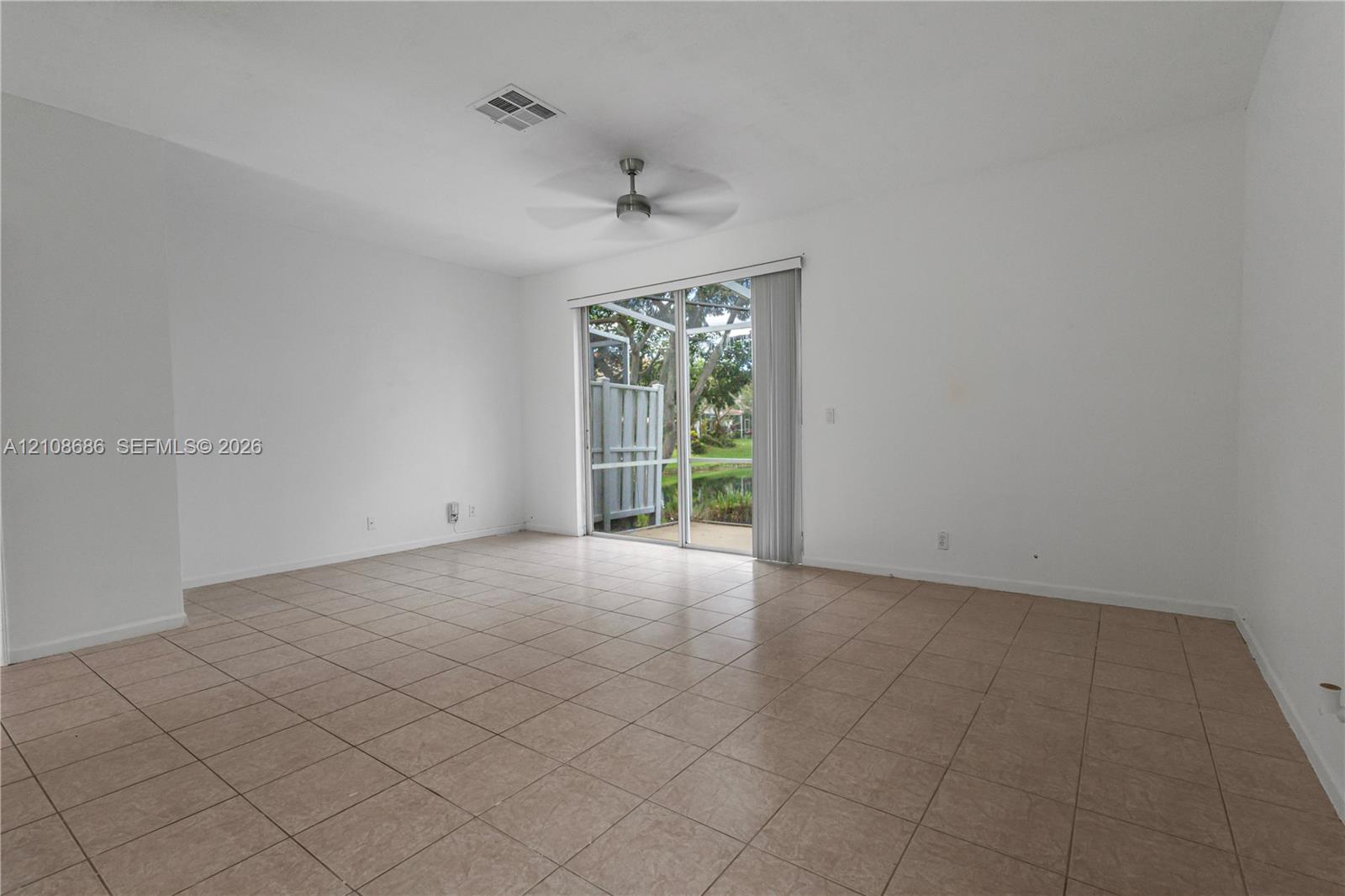 Interior space featuring neutral-toned tile flooring, a ceiling fan, and sliding glass doors that open to an outdoor screened enclosure Interior space featuring neutral-toned tile flooring, a ceiling fan, and sliding glass doors that open to an outdoor screened enclosure