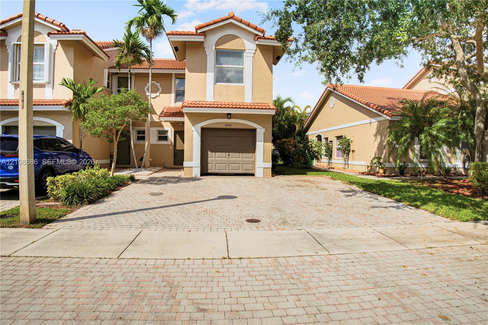 Stucco exterior with a tiled roof, attached garage, and paved driveway Stucco exterior with a tiled roof, attached garage, and paved driveway