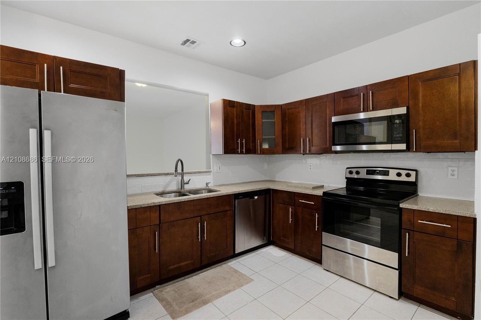 Kitchen featuring stained wood cabinetry, stone countertops, stainless steel appliances, and a double-basin stainless steel sink with a high-arch faucet Kitchen featuring stained wood cabinetry, stone countertops, stainless steel appliances, and a double-basin stainless steel sink with a high-arch faucet