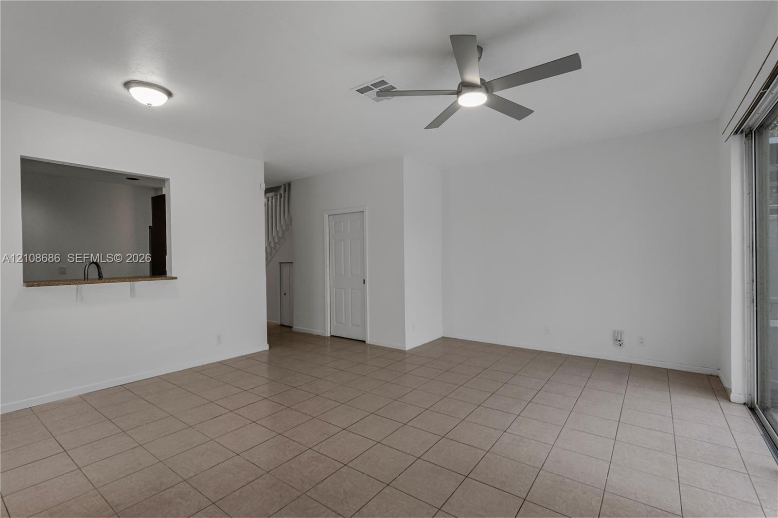 Neutral tile flooring, ceiling fan with integrated lighting, pass-through opening to kitchen, and sliding glass door Neutral tile flooring, ceiling fan with integrated lighting, pass-through opening to kitchen, and sliding glass door