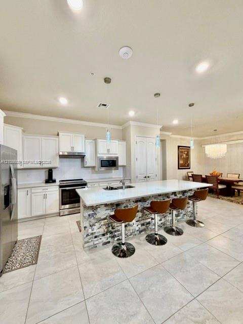 Kitchen featuring white cabinetry, stone-veneer island base, quartz countertops, stainless steel appliances, and large-format tile flooring