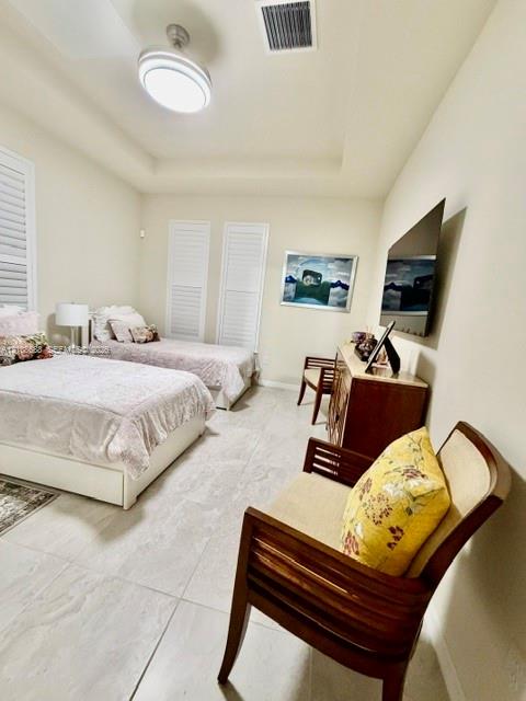 Tray ceiling featuring a central flush-mount light fixture, stone-finish tile flooring, and plantation shutters