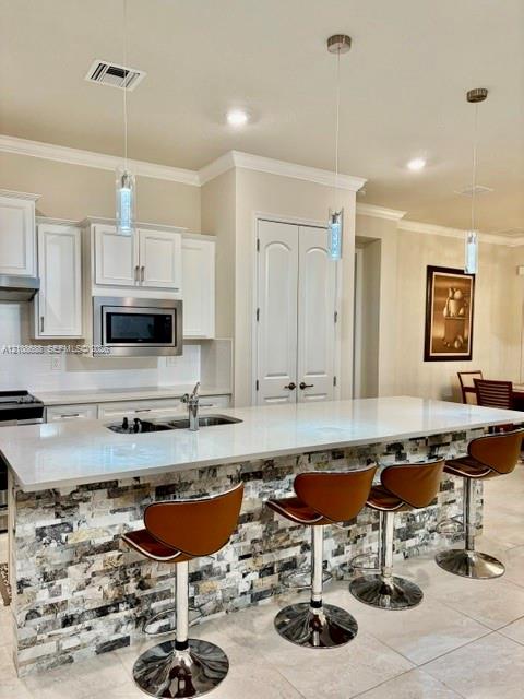 Kitchen featuring white cabinetry, solid surface countertops, a stone-veneer island facade, and triple pendant lighting