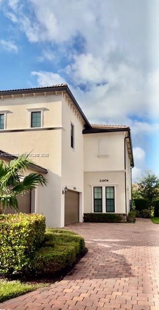 Two-story stucco exterior featuring a tile roof, decorative corbel accents, multi-pane windows with trim detailing, and a multi-car garage with a paved driveway