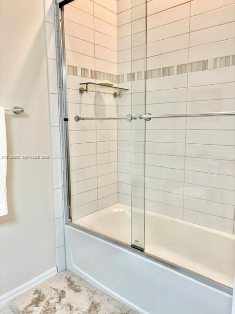 Bathtub enclosure featuring white horizontal subway-style wall tile, a glass sliding shower door with chrome hardware, an integrated glass corner shelf, and a decorative mosaic accent border