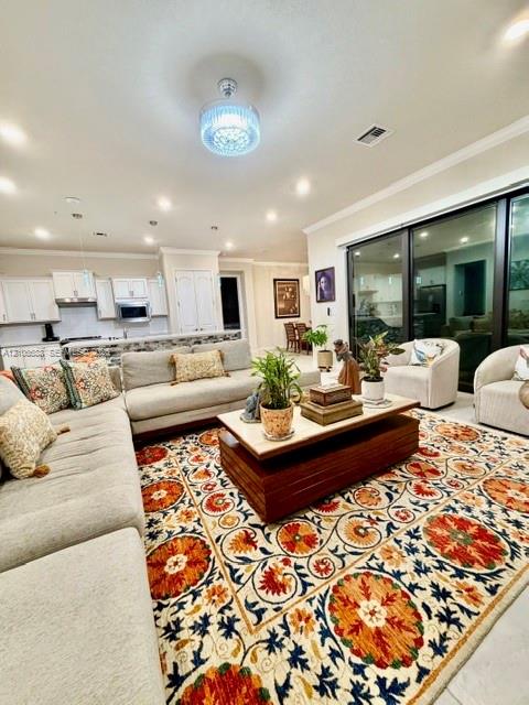 Open-concept interior featuring recessed lighting, crystal-accented flush-mount chandelier, crown molding, and expansive multi-panel sliding glass door