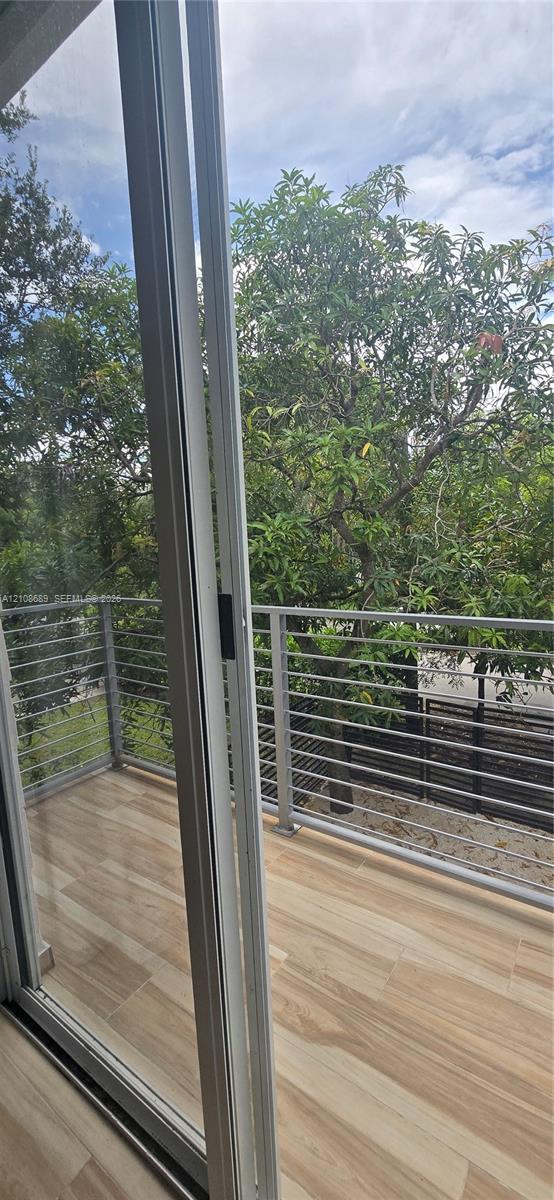 Balcony featuring wood-finish tile flooring, metal horizontal-bar railing, and floor-to-ceiling glass sliding doors Balcony featuring wood-finish tile flooring, metal horizontal-bar railing, and floor-to-ceiling glass sliding doors