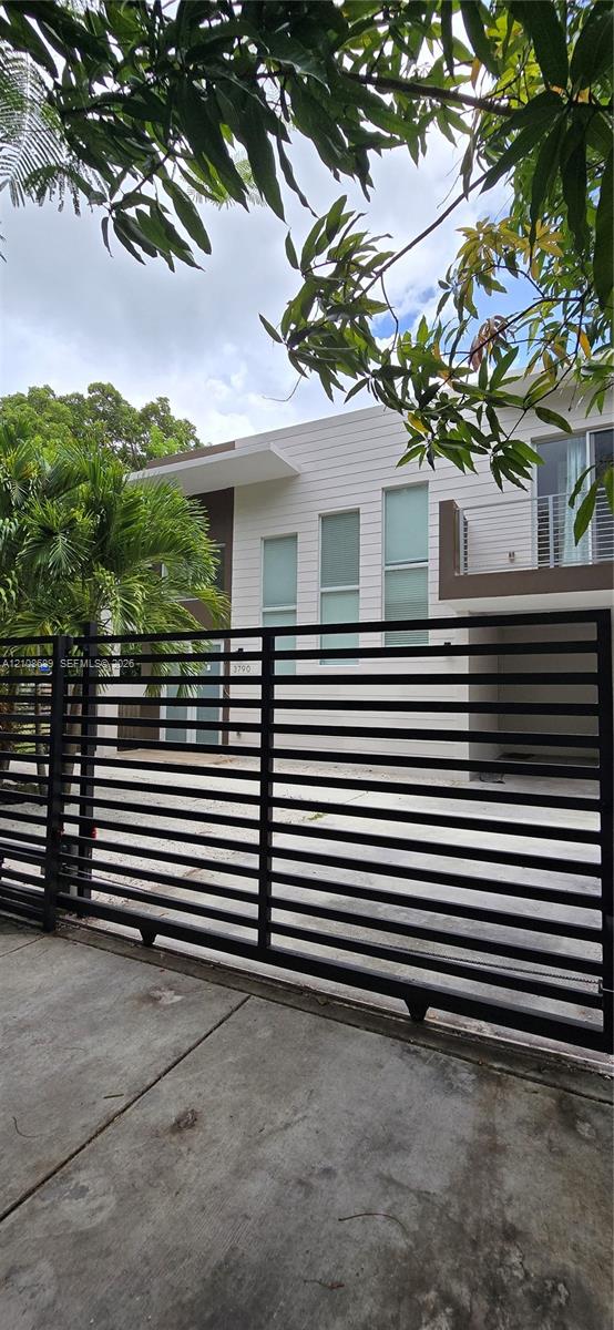 Modern two-story exterior featuring horizontal siding, a private gated entrance, tall vertical windows, and a metal-railing balcony
