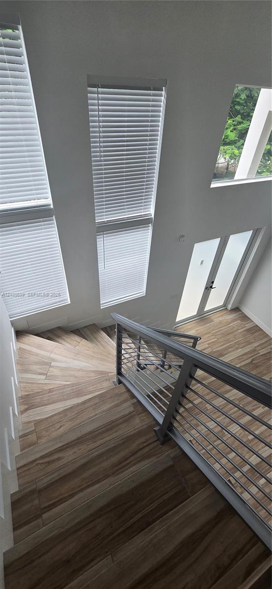 Staircase featuring wood-finish flooring, metal cable railing, floor-to-ceiling windows, and frosted glass paneled door