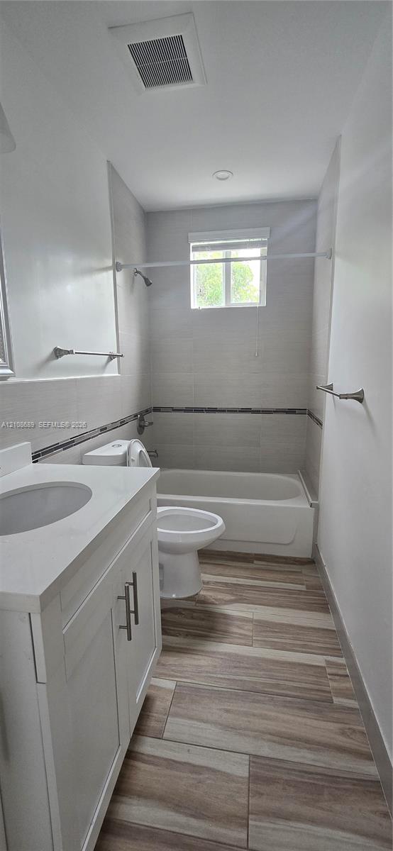 White vanity with a stone-finish countertop, wood-finish tile flooring, and tiled shower surround with decorative mosaic accent White vanity with a stone-finish countertop, wood-finish tile flooring, and tiled shower surround with decorative mosaic accent