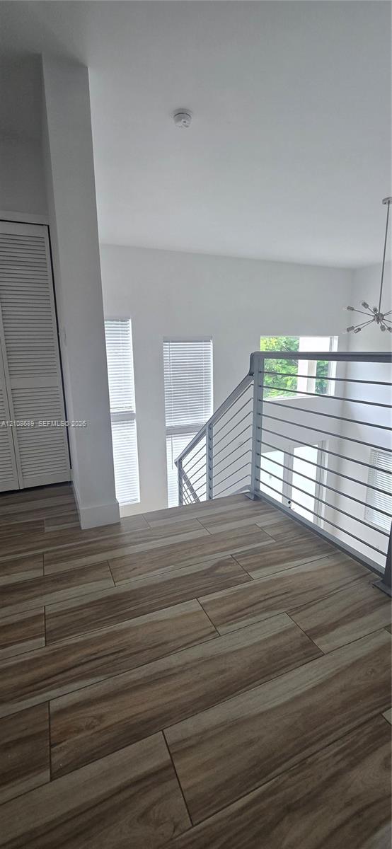 Landing area featuring wood-finish flooring, a horizontal cable railing system, tall windows, and a closet with louvered doors Landing area featuring wood-finish flooring, a horizontal cable railing system, tall windows, and a closet with louvered doors