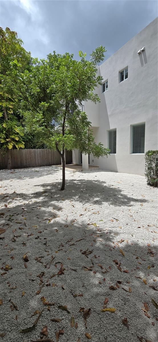 Exterior yard space featuring a white gravel ground cover, mature landscaping, and a wood-slat privacy fence