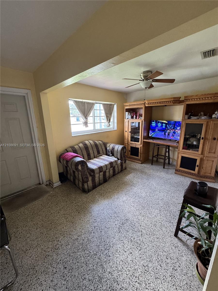 Living space featuring built-in wooden cabinetry, multi-pane window, ceiling fan with light fixture, and terrazzo flooring