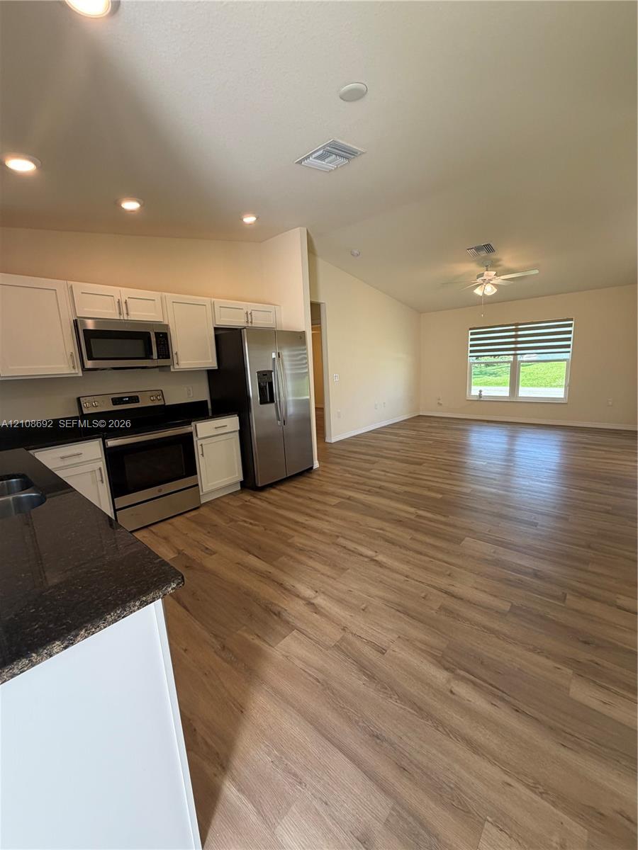 Kitchen featuring white shaker-style cabinetry, dark stone countertops, stainless steel appliances, and wood-finish flooring throughout