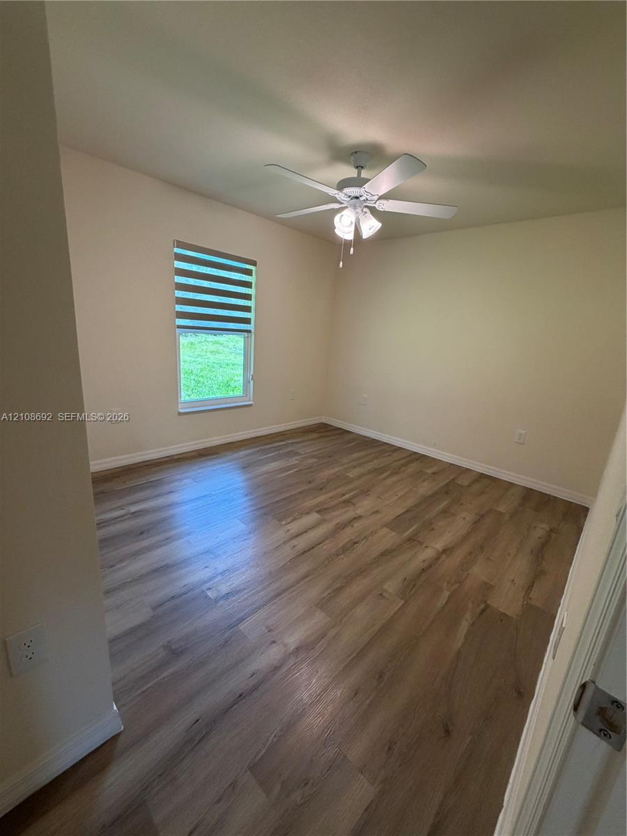 Wood-finish flooring, ceiling fan with integrated light fixture, and a single-hung window featuring a horizontal banded shade