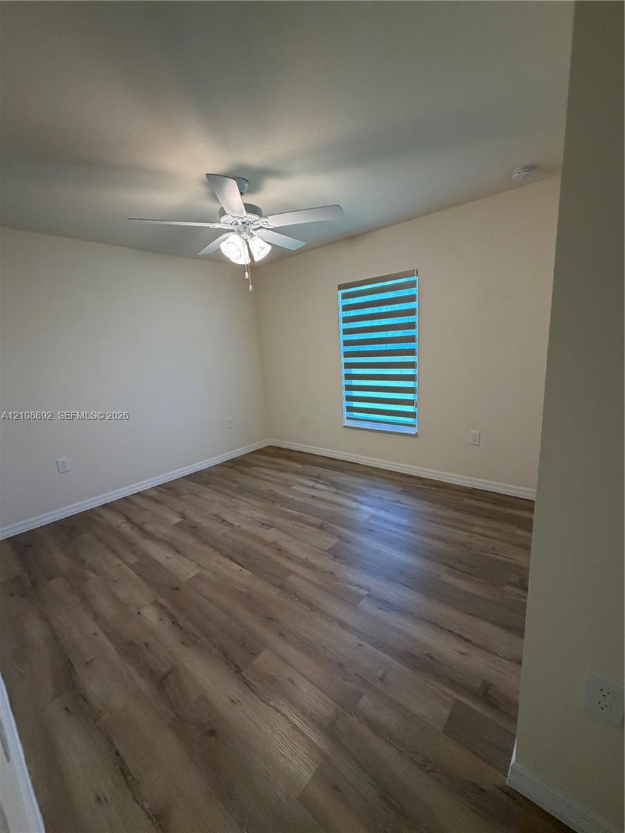 Room interior featuring wood-finish flooring, a ceiling fan with integrated lighting, and a window with horizontal shade treatment
