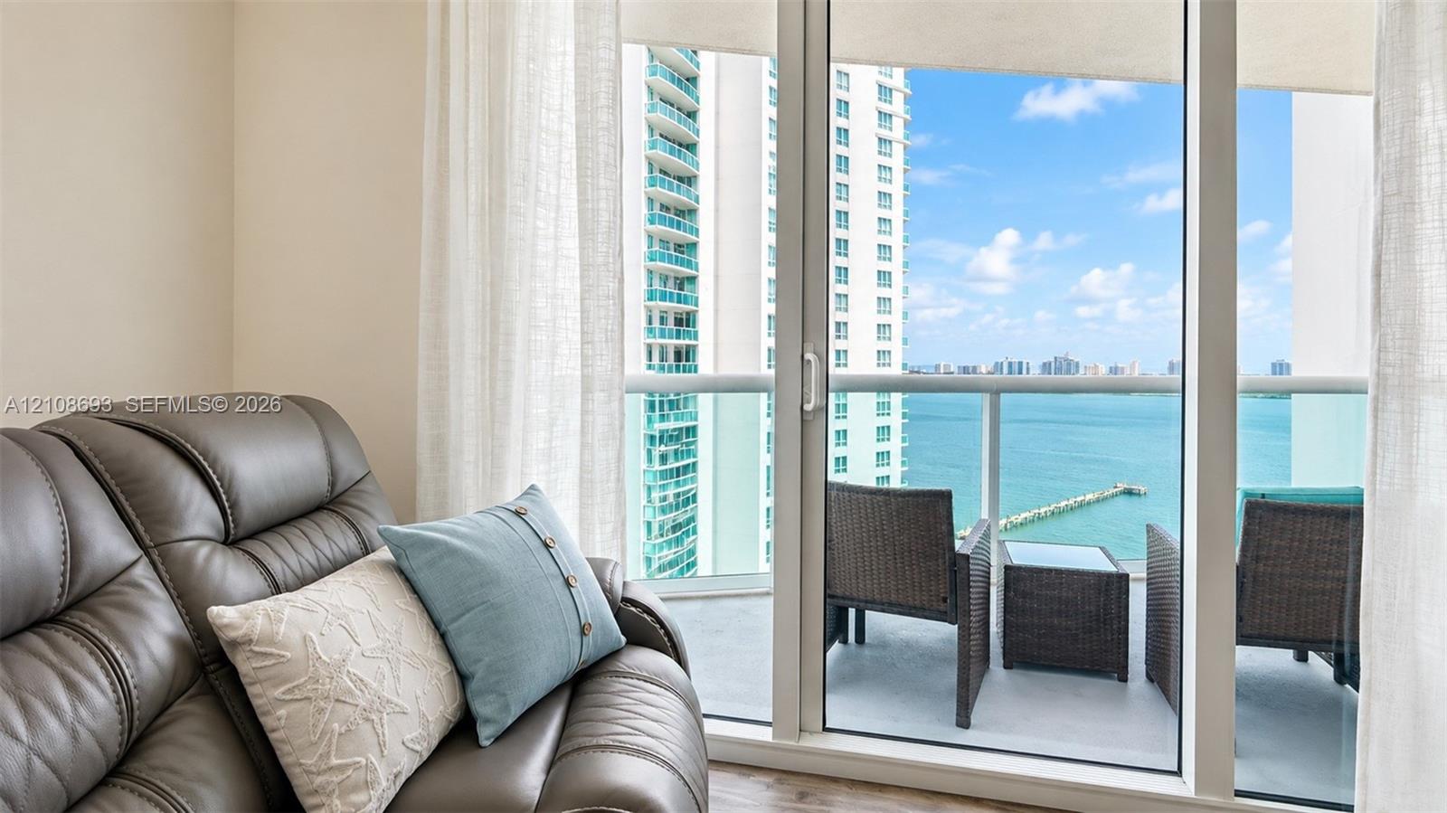 Floor-to-ceiling sliding glass door providing external access to a balcony with a glass railing and waterfront scenery