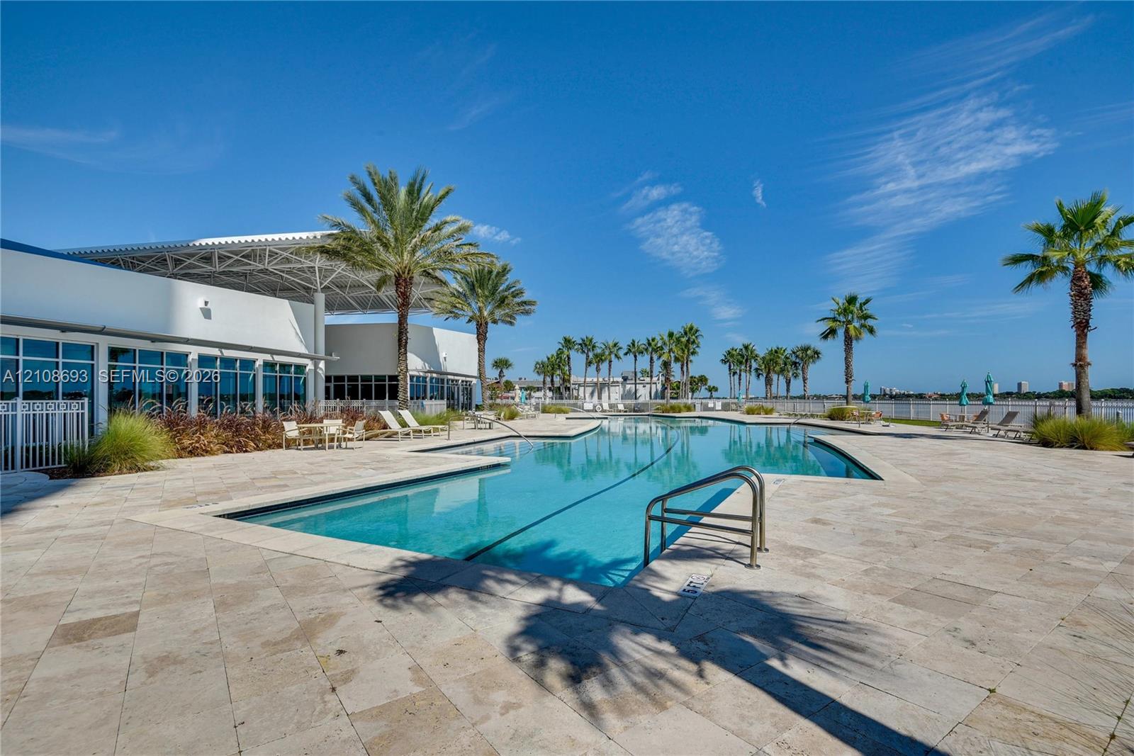Swimming pool with integrated steps, surrounded by a stone-paved deck and palm trees