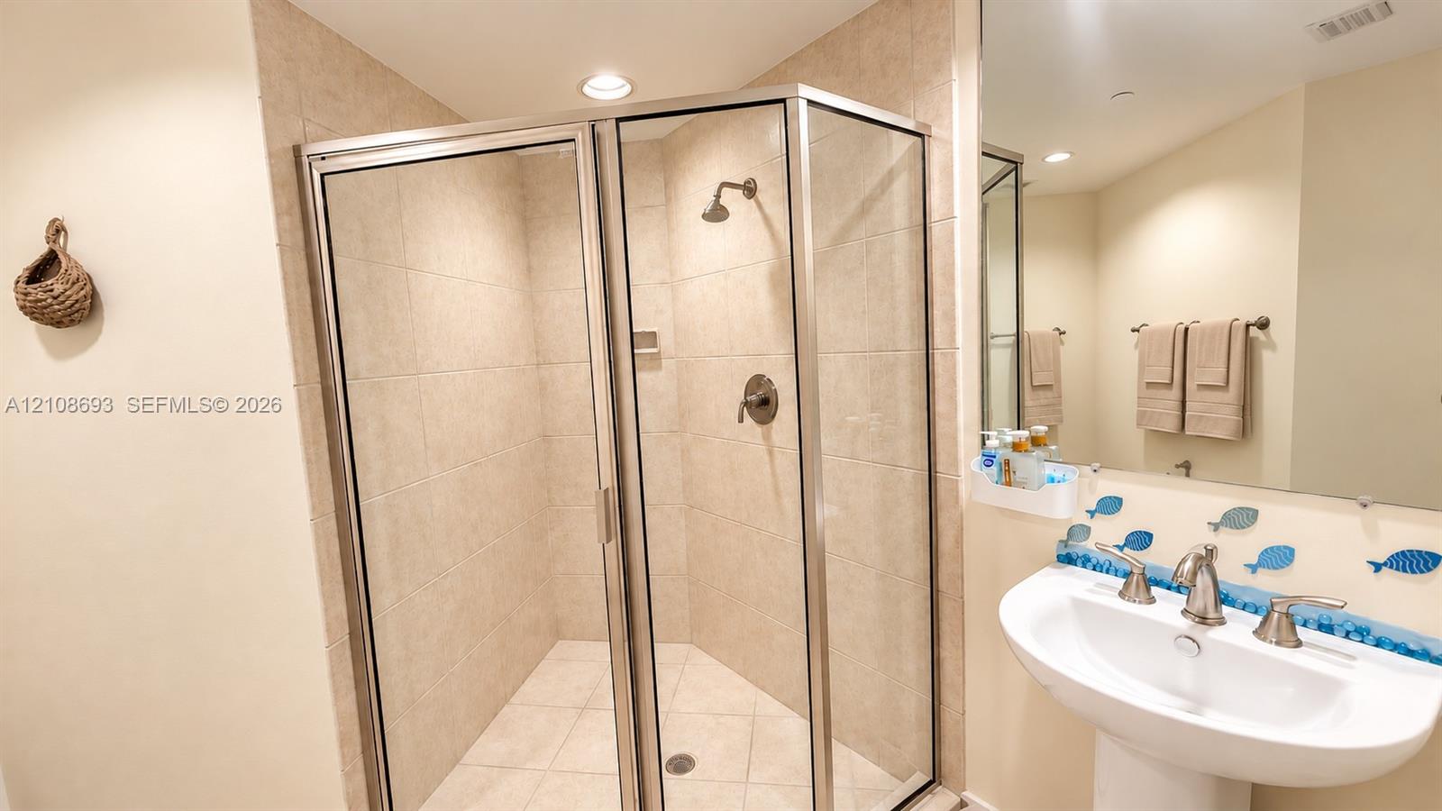 Walk-in corner shower with a glass enclosure, ceramic tile surround, pedestal sink with metallic fixtures, and a wall-mounted mirror