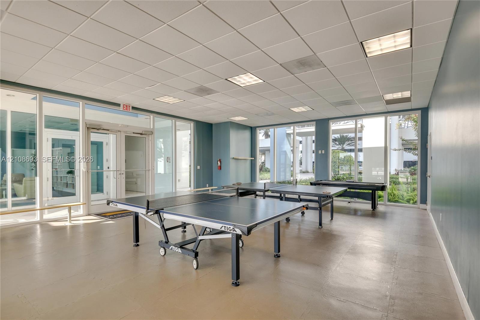 Open-concept multi-use space featuring full-height glass walls, recessed drop-ceiling grid lighting, and durable flooring