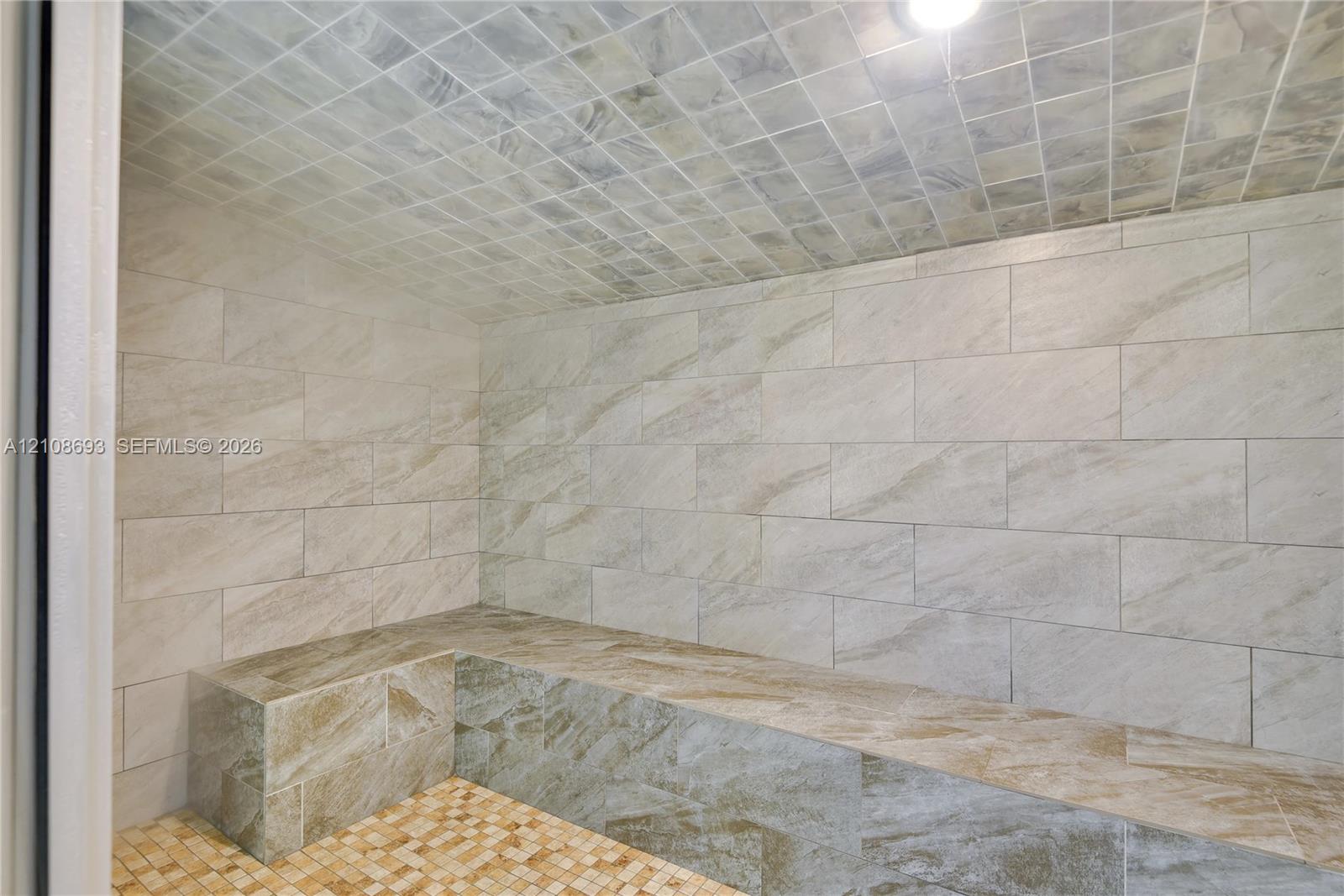 Enclosed sauna featuring large-format stone-style wall tile, a built-in stone-style bench, mosaic-tile flooring, and a tiled vaulted ceiling