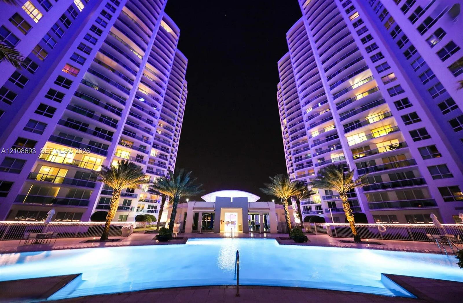 Swimming pool with surrounding paver deck, palm trees, and high-rise tower exteriors featuring expansive balconies
