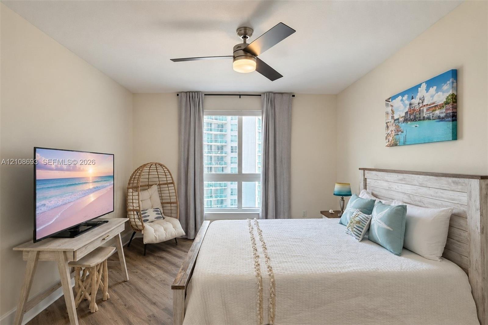 Wood-finish flooring, multi-pane window with neutral drapery, and a contemporary ceiling fan with integrated lighting