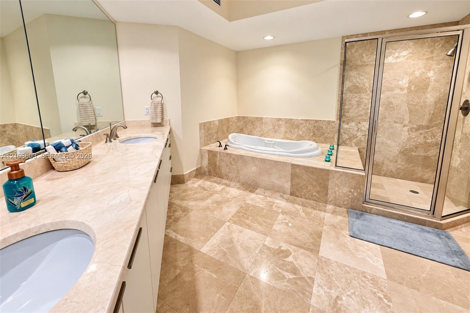 Bathroom featuring natural stone tile flooring, an expansive vanity with stone countertop, an inset soaking tub, and a separate glass-enclosed shower