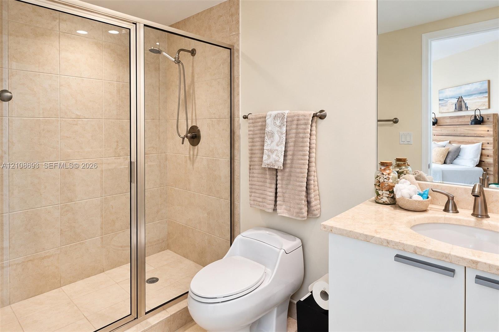 Bathroom featuring a glass-enclosed shower with neutral wall tiling, stone-surface vanity countertop, undermount sink, and metal-finish plumbing fixtures