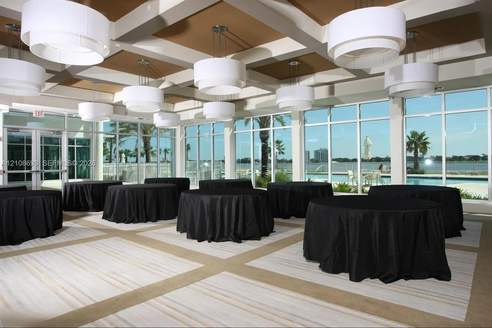 Coffered ceiling with tiered drum pendant lighting, floor-to-ceiling windows, and wall-to-wall carpeting