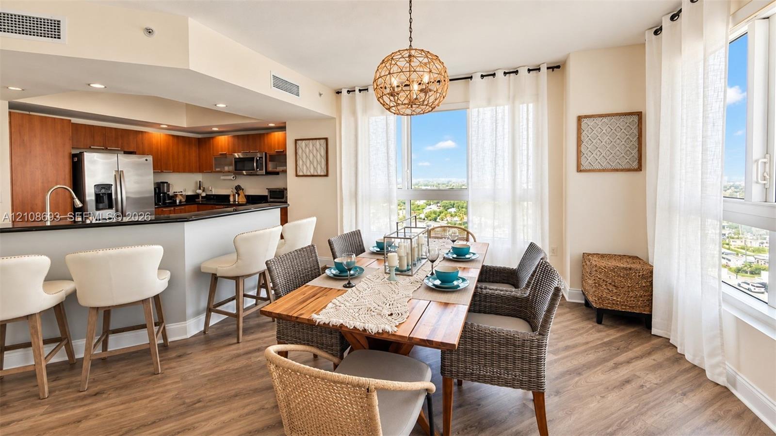 Open-concept kitchen and dining area featuring wood-finish flooring, a kitchen island with stone countertop, stainless steel appliances, and floor-to-ceiling windows