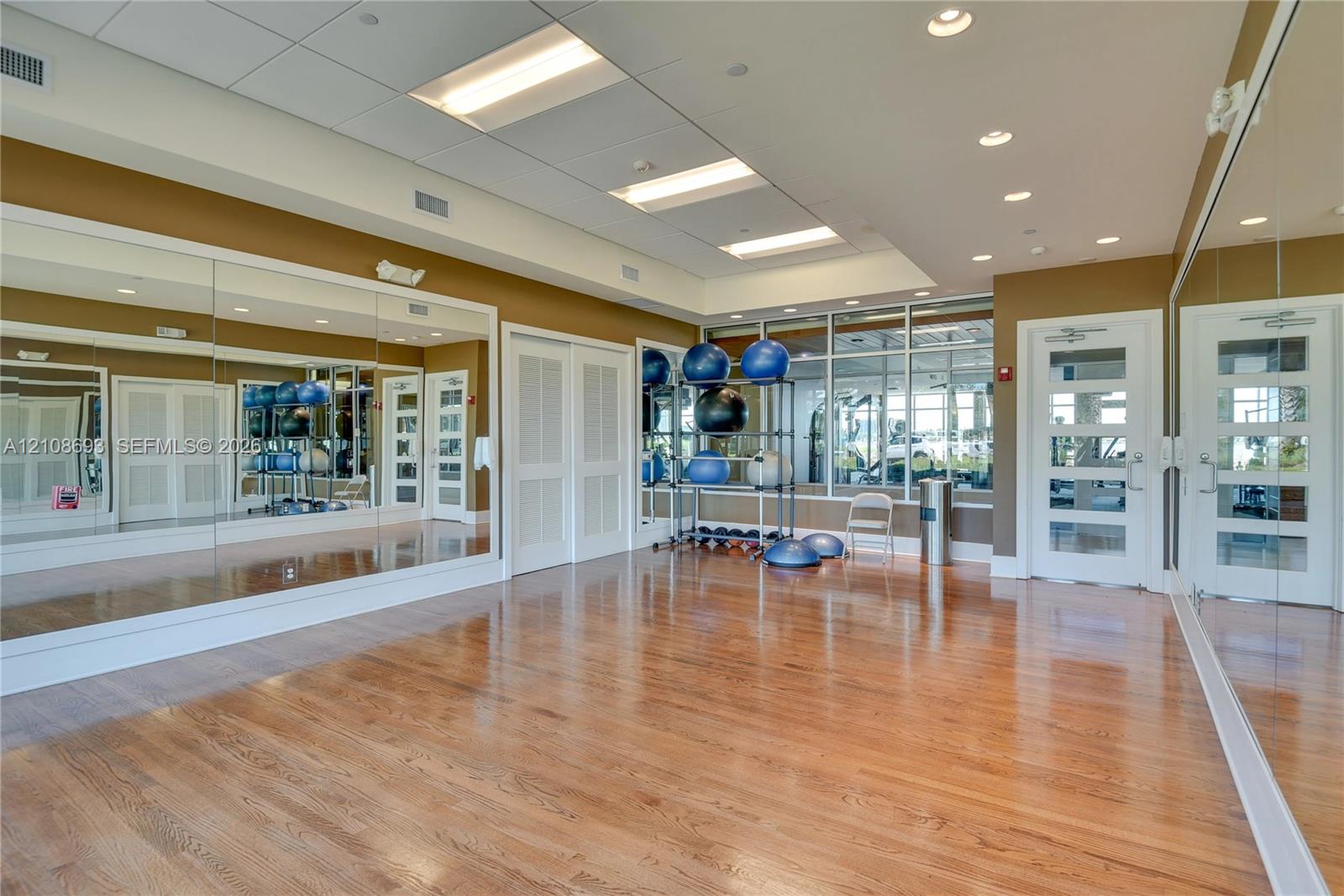 Fitness studio featuring wood-finish flooring, extensive wall-mounted mirrors, recessed lighting, and large windows