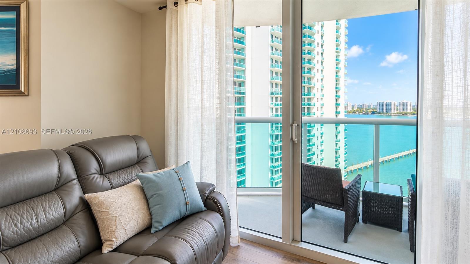 Full-height sliding glass doors with access to a private balcony featuring a glass railing and water backdrop