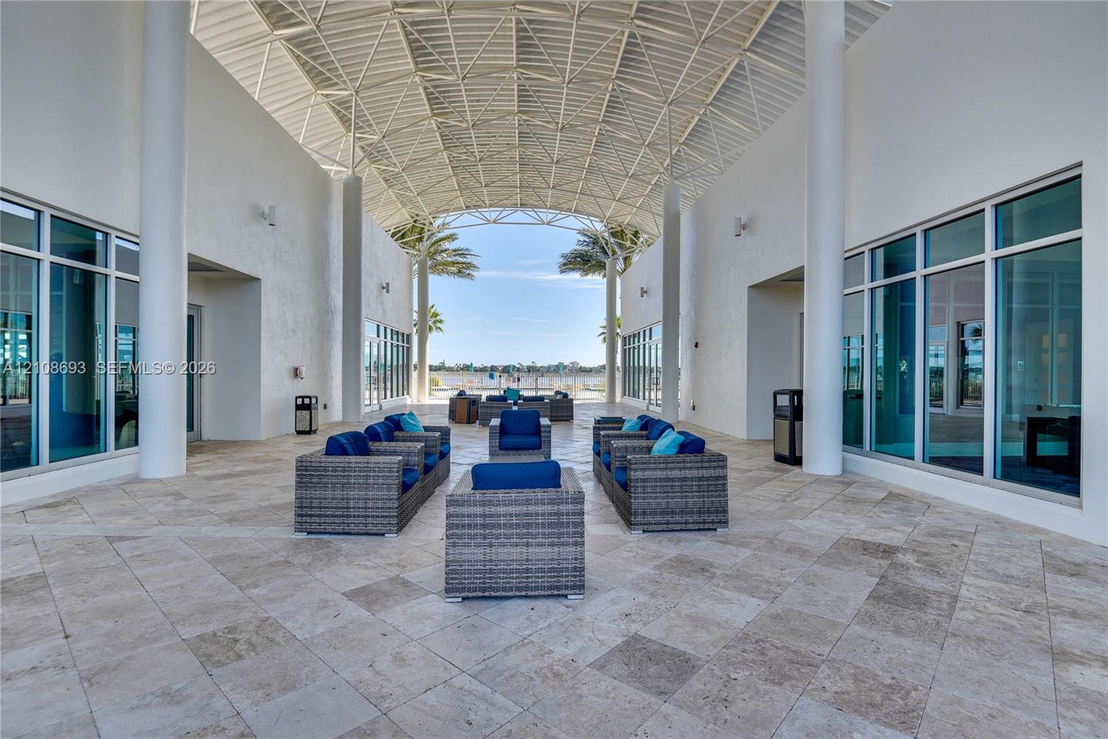 Covered open-air pavilion featuring an expansive vaulted lattice ceiling, structural columns, stone tile flooring, and floor-to-ceiling glass windows