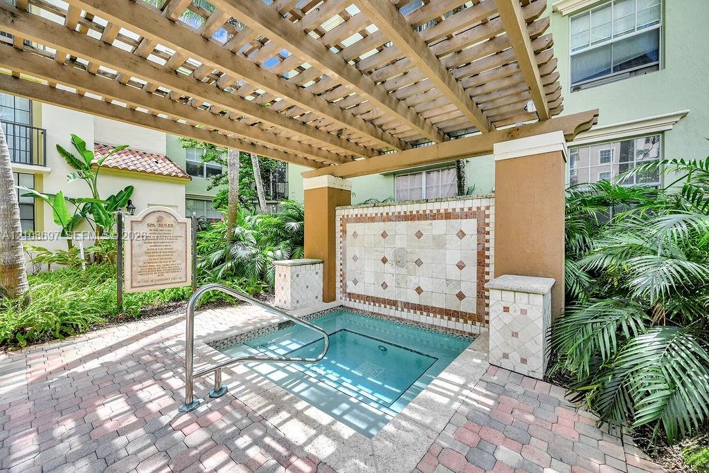 Spa area featuring a stone-tiled accent wall, overhead wooden pergola, brick paver decking, and metal handrail