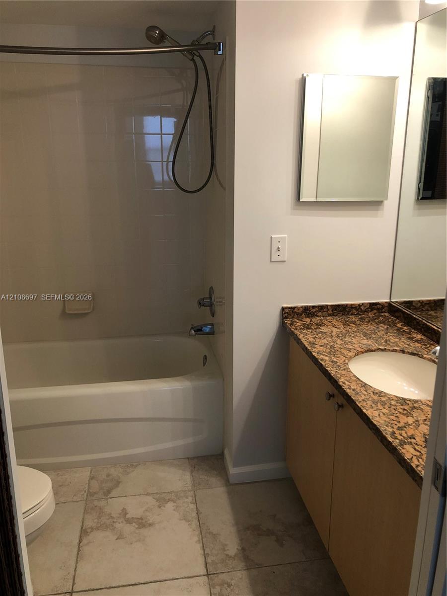 Bathroom featuring a tub-shower combination with tiled wall surround, vanity with stone-finish countertop and integrated sink, large wall-mounted mirror, and tile flooring