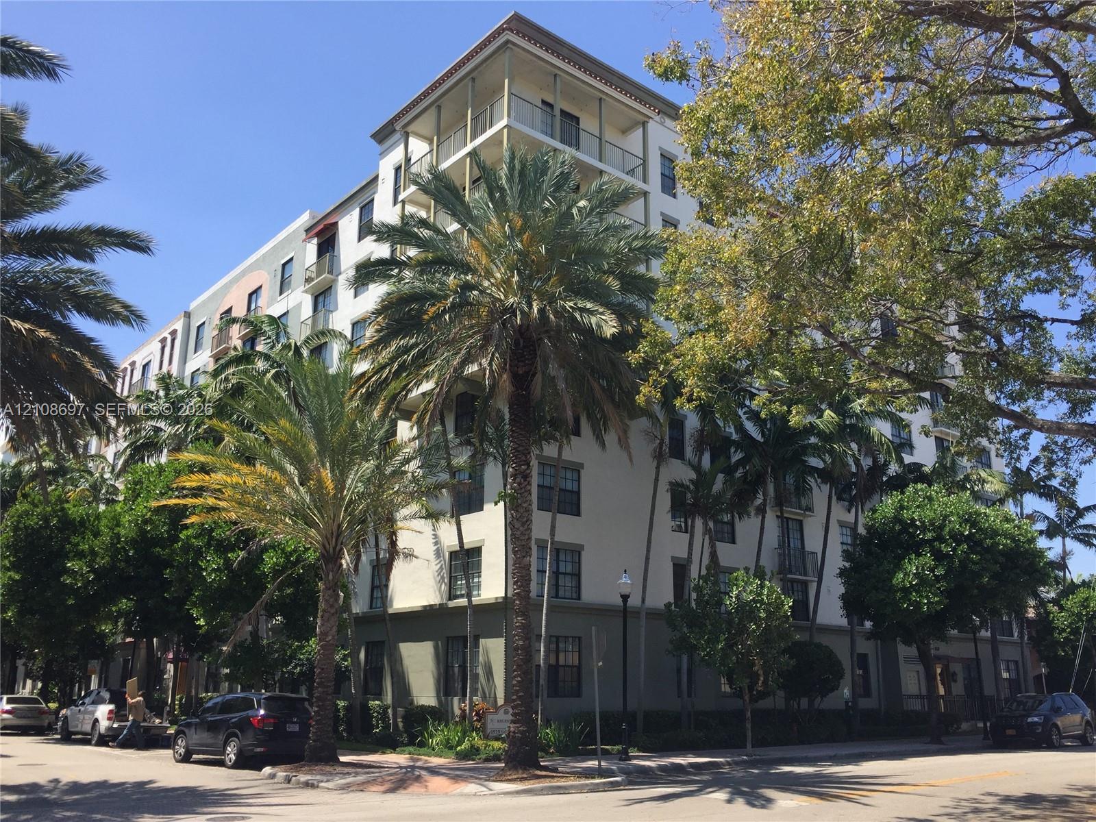 Multi-story residential building featuring a light-toned stucco facade, private balconies, and mature palm tree landscaping
