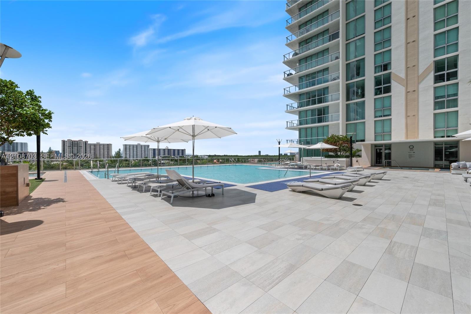 Elevated swimming pool featuring stone tile decking, wood-finish flooring accents, and a glass panel railing