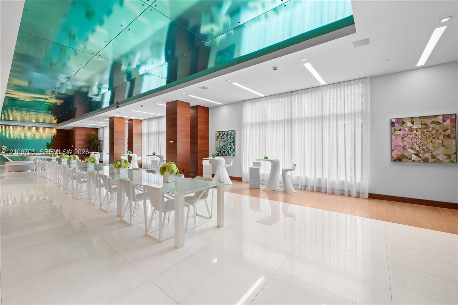 Large-format polished tile flooring, reflective blue-tinted ceiling paneling, floor-to-ceiling windows with integrated drapery, wood-finish wall paneling, and recessed linear lighting