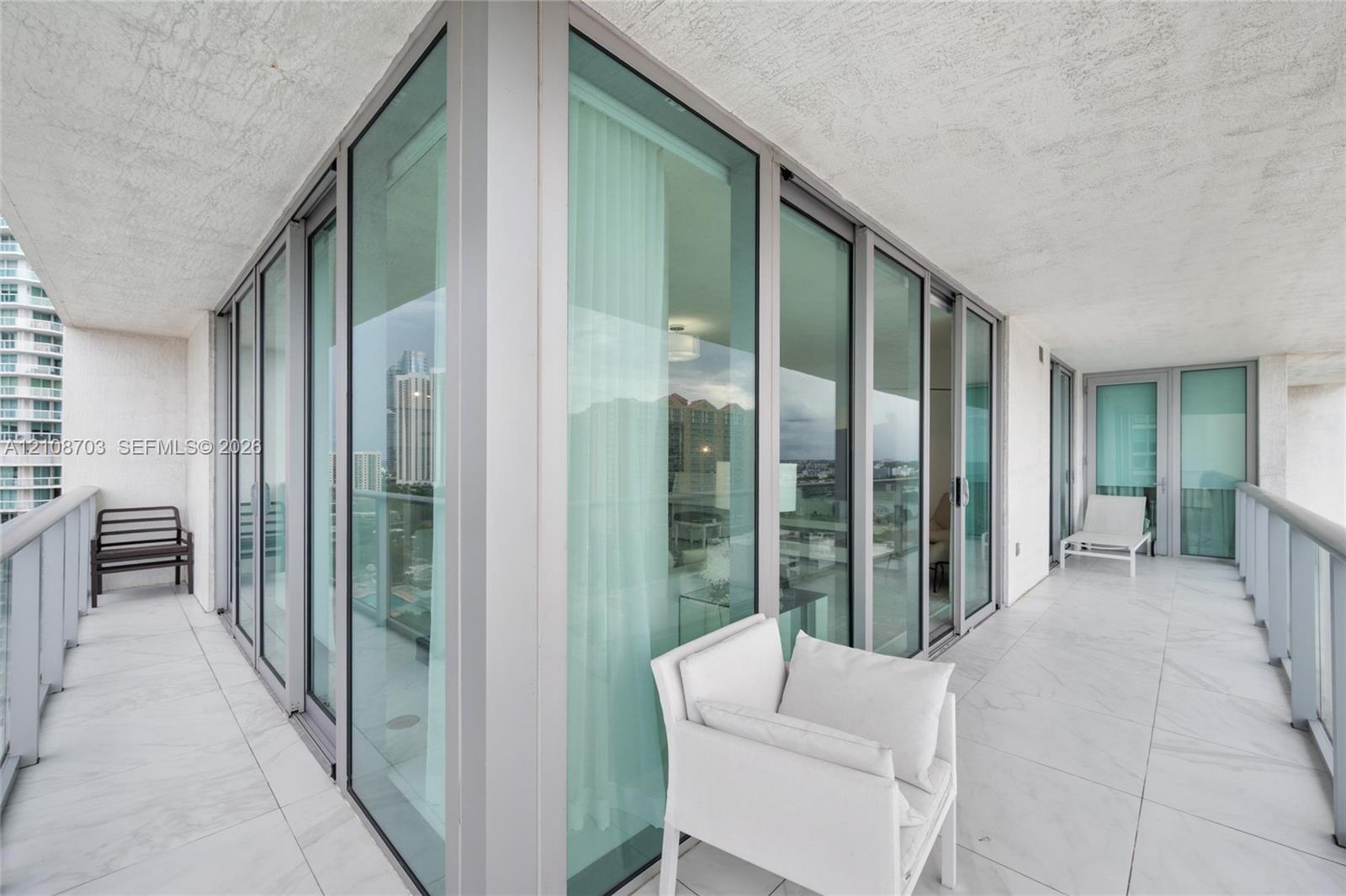 Wrap-around balcony featuring large-format tile flooring, floor-to-ceiling glass panel sliding doors, and metal railings