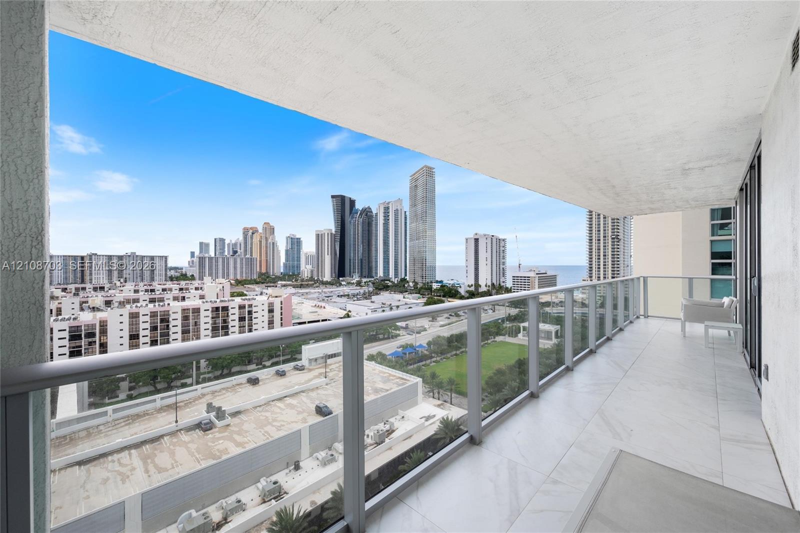 Private covered balcony featuring large-format stone-finish flooring and a glass panel railing overlooking the urban skyline